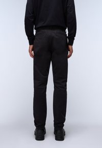 Pantaloni neri in cotone con taglio dritto, cintura elasticizzata e due tasche posteriori. Indossati con scarpe nere, visti da dietro.