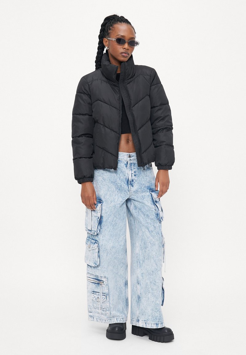 Chaqueta de plumas en negro, con un cuello alto y un diseño acolchado. Combinada con unos pantalones cargo holgados en azul claro, que cuentan con múltiples bolsillos.