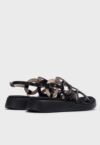 Sandalias negras con suela de plataforma, que presentan recortes circulares y una correa ajustable. Fabricadas en cuero suave con un acabado mate.