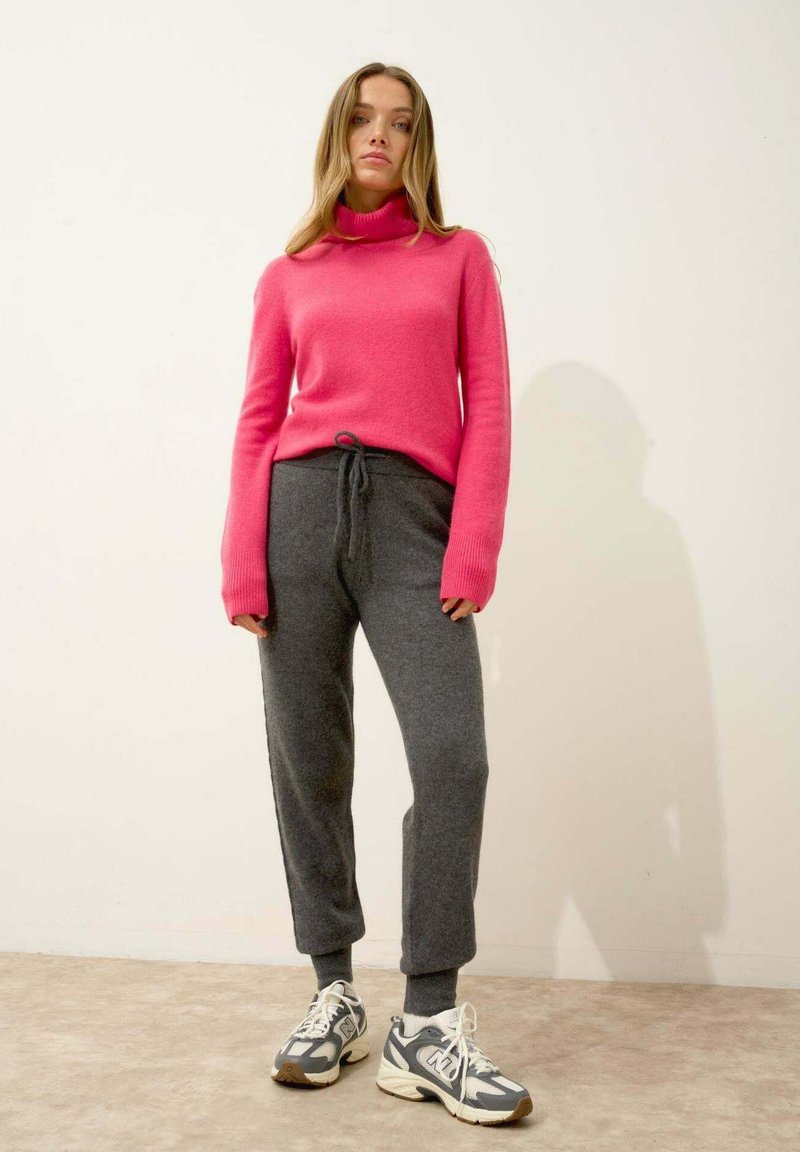 Rosa stickad turtleneck-tröja ihop med grå dragkedje-sweatpants och grå sneakers med vita detaljer. Slät yta, avslappnad passform.
