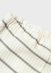 Randigt bomullstyg i off-white med tunna grå linjer. Har en ribbad yta och en vit knapp vid midjan.