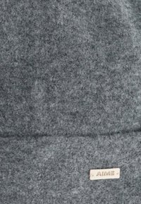 Tessuto feltro grigio, morbido al tatto, forma rettangolare con dettagli cuciti, caratterizzato da un piccolo etichetta metallica incisa con la parola "AIME."