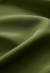 Textúrovaná olivovo zelená látka, hladká na dotyk, s jemným leskom a nežnými záhybmi, ktoré ilustrujú jej ľahkosť a flexibilné vlastnosti.