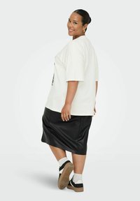 Camiseta blanca de algodón de gran tamaño con mangas cortas, combinada con una falda negra de imitación cuero. Zapatillas en blanco y negro con suelas grises.