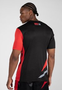 Korte mouwen sportshirt met een zwart lichaam, rode mouwen en grijze accenten. Bevat een logo op de achterkant en tekst langs de zijkant. Soepele stoffen textuur.