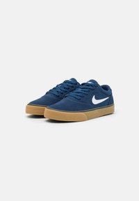 Baskets en daim bleu avec une semelle en caoutchouc, présentant le logo Nike en blanc, fermeture à lacets et dessus lisse et texturé.