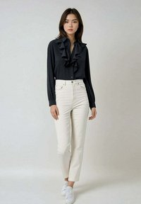 Blouse noire à volants avec des boutons, manches longues, associée à un jean droit taille haute blanc et des baskets blanches. Texture de tissu lisse.