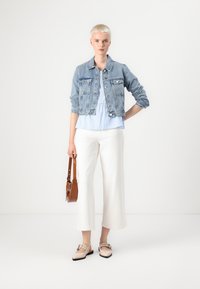 Chaqueta de denim azul claro, blusa blanca de peplum con cuadros azules, pantalones anchos blancos, zapatos planos beige y bolso cruzado marrón.