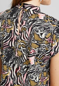 Blouse à manches courtes présentant un motif animalier coloré en noir, rose, jaune et blanc ; comprend un détail d'encolure clé avec des boutons.