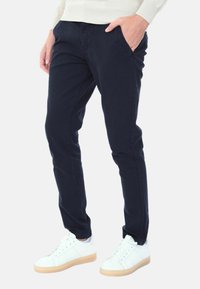 Chinos in cotone blu navy con vestibilità slim, tasche laterali e leggera elasticità. Abbinati a sneakers bianche con suola in gomma.