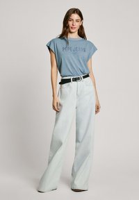 Šviesiai mėlyna trumpomis rankovėmis marškinėliai su "Pepe Jeans London" logotipu, derinami su aukštu liemeniu, plačiais šviesiai mėlynais džinsais ir juodu diržu.