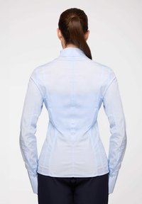 Camicia fitted azzurro chiaro con maniche lunghe, colletto alto e texture liscia. Presenta polsini a bottone e cuciture verticali per una migliore sagomatura.