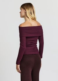 Bordeauxrotes, schulterfreies, geripptes Oberteil mit langen Ärmeln, das eine figurbetonte Passform und eine geraffte Detailverarbeitung an der Taille aufweist, kombiniert mit dunkelbraunen Hosen.