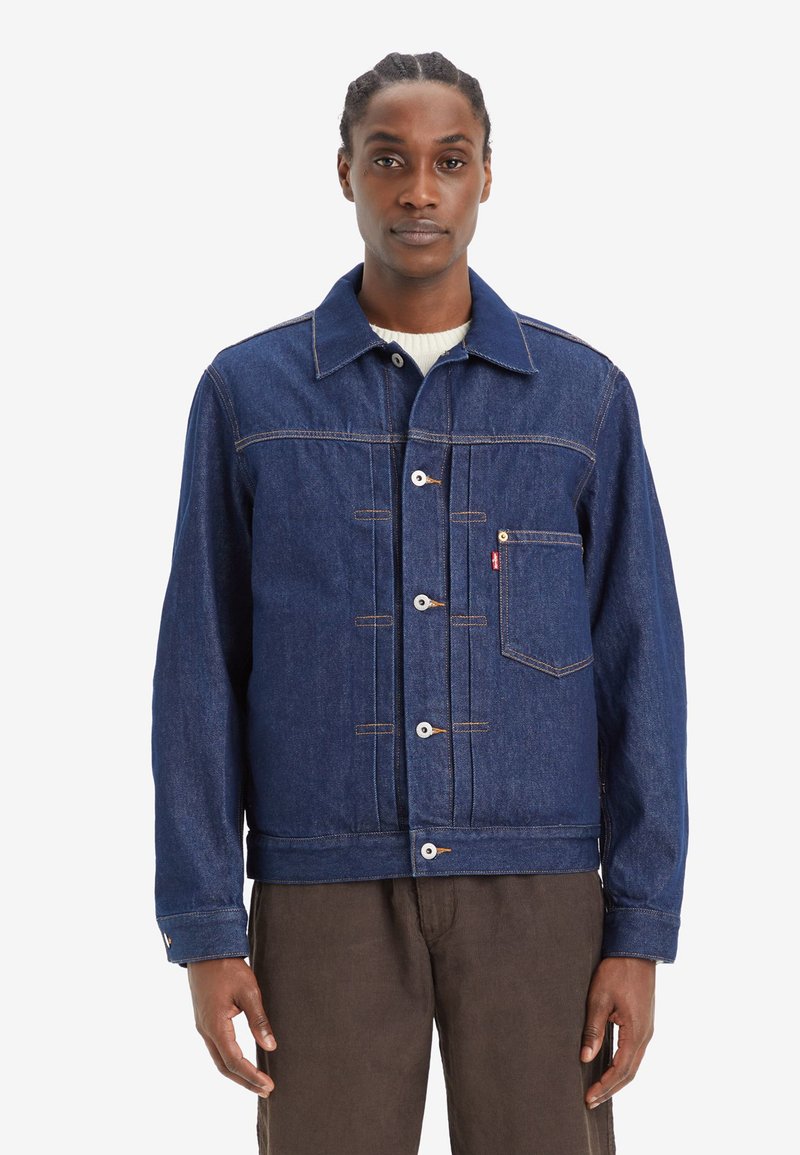 Dunkelblaue Jeansjacke mit Knopfvorn, Brusttasche und kontrastierenden gelben Stichen. Aus Baumwollmaterial mit strukturiertem Schnitt.
