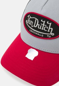 Grå och röd keps med böjd skärm, prydd med en svart och vit broderad "Von Dutch Originals"-logotyp framtill och en etikett på skärmen.