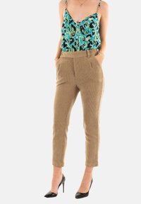 Pantaloni in corduroy beige con silhouette aderente, tasche frontali e vita alta, abbinati a un top blu con fantasia e tacchi neri.