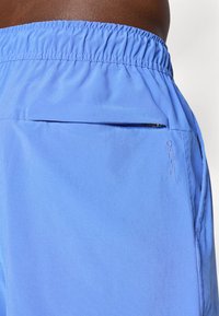 Blå atletiske shorts lavet af letvægtsstof. Har en elastisk talje og en lynlåslomme på siden. "DRI-FIT" logoet er broderet på siden.