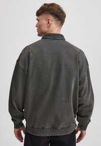 Herren Oversized-Sweatshirt in Dunkelgrau mit Kragen, gerippten Bündchen und Saum. Es besticht durch einen strukturierten Stoff und hat abfallende Schultern.