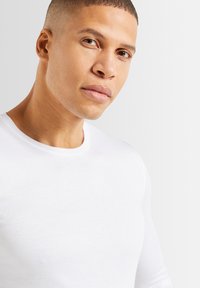 Weißes Langarm-T-Shirt aus weichem Stoff mit rundem Ausschnitt. Der Schnitt ist schmal und betont eine glatte Textur und klare Linien.