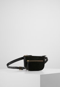 Musta nahka- ja mokkanahkainen vyölaukku, jossa pyöreä muoto, kullanvärinen vetoketju ja säädettävä hihna. Siinä on yksi etutasku vetoketjulla ja hapsukoriste.