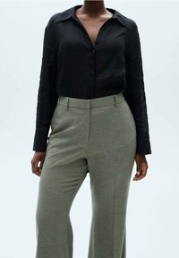 Czarna lniana koszula na guziki z kołnierzykiem, w połączeniu z jasnoszarymi spodniami w kratę. Stylizacja charakteryzuje się luźnym krojem i gładką teksturą.