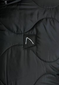 Crna jakna s kvadratnim prešanim uzorkom koja ima glatku, sjajnu teksturu. Uključuje kvadratnu oznaku s minimalističkim bijelim logotipom. Cijela jakna ima zaobljen uzorak prešanja.