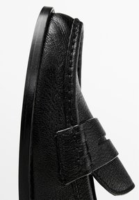 Schwarzer Lederschuh mit strukturiertem Finish, ausgestattet mit einem breiten Riemen und einer rechteckigen Schnalle sowie einer flachen, glatten Sohle.