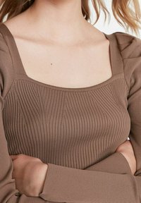 Braun gestreiftes Langarmoberteil mit quadratischem Ausschnitt und strukturierten Details. Der Stoff wirkt weich und enganliegend, betont die Körperform.
