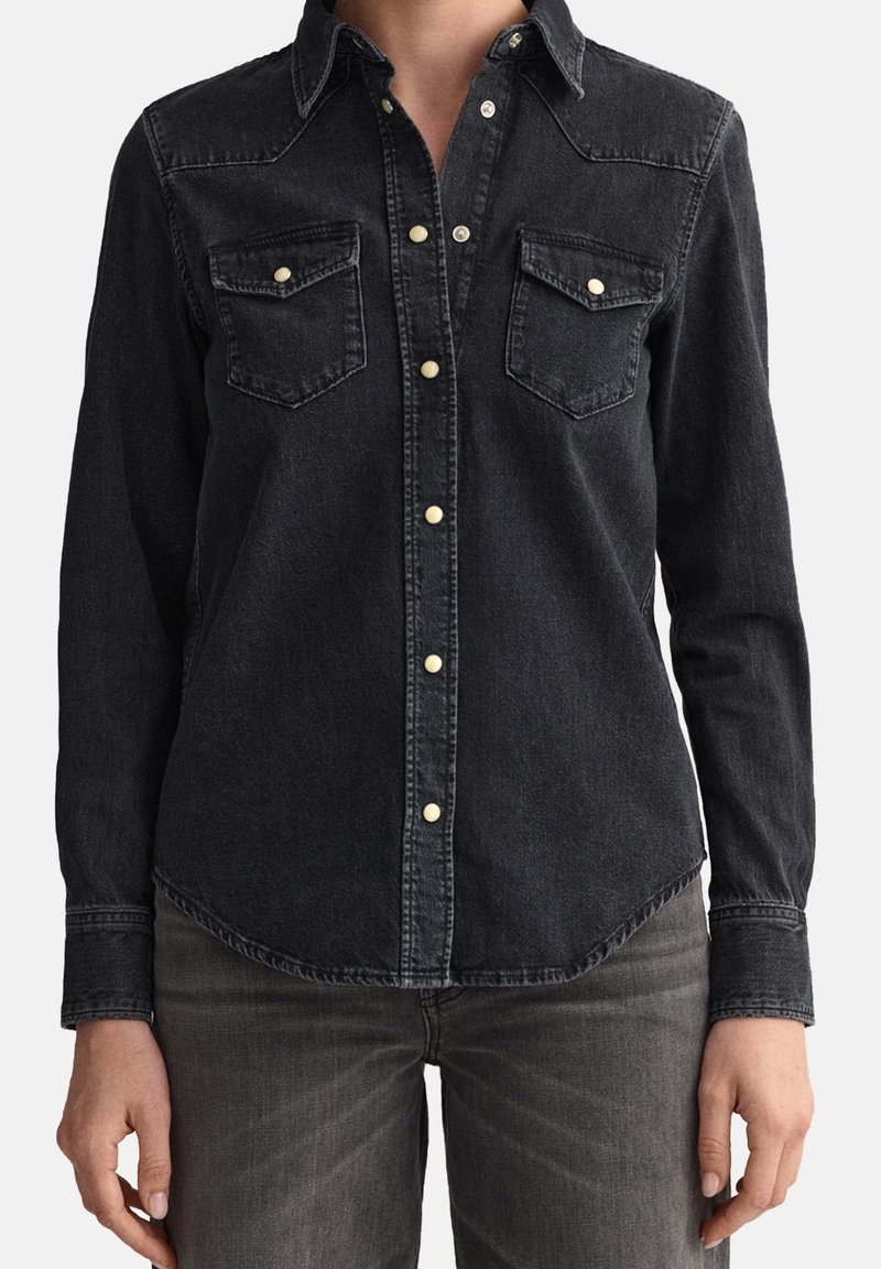 Chemise en denim noire à manches longues, col pointu et deux poches poitrine. Présente des boutons de couleur claire et un ourlet arrondi.
