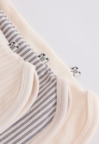 Three soft baby bodysuits in cream and striped gray, showing close-up of shoulders and brand tags with heart symbols.