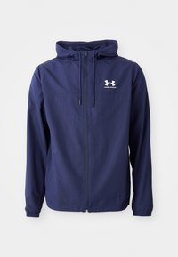 Veste à capuche bleu marine avec fermeture éclair à l'avant, cordons ajustables, poignets élastiques et logo blanc Under Armour sur la poitrine gauche.