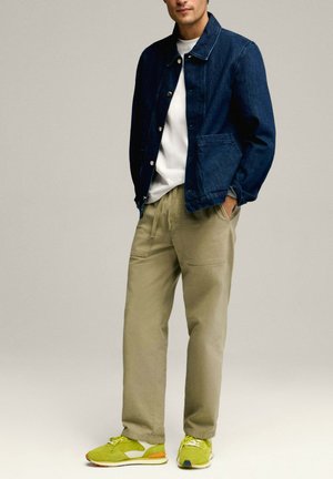 Donkerblauwe denimjack met knoopsluiting, witte shirt, kaki broek en groene sneakers met grijze en oranje accenten. Casual pasvorm.