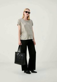 Μεταλλικό τοπ κοντό μανίκι με κατακόρυφες ρίγες, σε συνδυασμό με μαύρα παντελόνια φαρδιάς γραμμής και μαύρη τσάντα. Μοντέλο φορά σκούρα γυαλιά ηλίου.