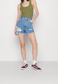 Grön, ribbade linne, högmidjade denimshorts med slitna detaljer och fransad nederkant, kombinerat med vinröda Vans-sneakers och vita crew-strumpor.
