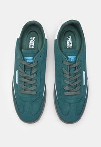Tumedat tealin värvides sneakerid sametise tekstuuriga, valged aktsendid kanna juures ja rohelised paelad. Kanna peal on "NORTH STAR" bränding.