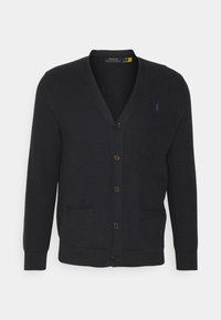 Marinblå kofta i texturerat stickat tyg, med V-ringning, fem knappar och två framfickor, med en logotyp på vänster bröst.