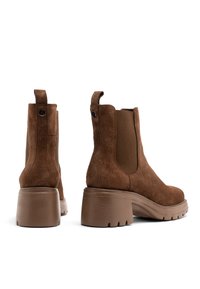 Brązowe zamszowe botki za kostkę z elastycznymi panelami bocznymi, pętelką do zakupu i masywnymi obcasami. Zawierają teksturowaną gumową podeszwę zapewniającą lepszą przyczepność.