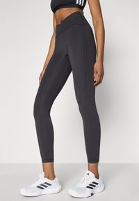 Mustad spordipüksid venivast kangast, millel on kõrge talje, voolujoonelised õmblused ja kehale sobiv lõige. Kombineeritud valgete tossudega.