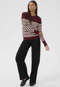 Pull à rayures bourgogne avec des lignes crème, col rond, poignets côtelés, associé à un pantalon noir à jambes larges et des mocassins noirs. Design simple.
