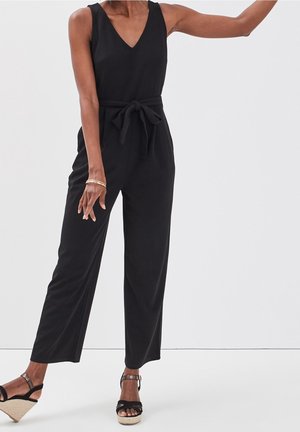Combinaison noire avec décolleté en V, sans manches, détail de taille nouée et coupe large. Tissu texturé avec une finition lisse.