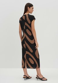 Schwarzes Kleid mit braunem abstraktem Muster, kurze Ärmel, knielange Länge, seitlicher Schlitz, glattes Material, kombiniert mit schwarzen Sandalen.