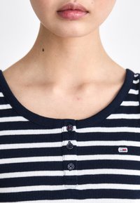 Navy and white striped ribbed top with a round neckline, three-button placket, and small logo accent on the left side.