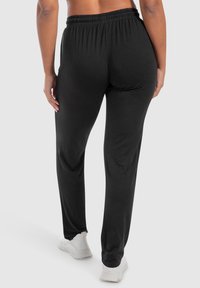 Zwarte sweatpants met een zachte textuur, een elastische tailleband en taps toelopende pijpen, gecombineerd met witte sneakers. Geen zichtbare patronen of hardware.