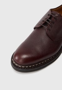 Dunkelburgunderfarbene Lederschuhe mit strukturierter Oberfläche, runder Zehenform und Schnürdesign. Mit einer kontrastierenden genähten Naht entlang der Sohle.