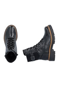 Paire de bottes de combat en cuir noir à lacets avec semelles robustes et boucle latérale, l'une vue du dessus, l'autre de côté sur fond blanc.