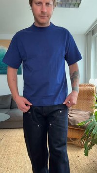 T-shirt de algodão azul com mangas curtas, combinada com jeans de ganga escuros com costura visível e metal prateado nos bolsos.