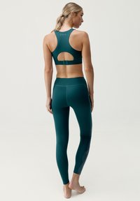 Zielony stanik sportowy z odkrytymi plecami, w połączeniu z pasującymi legginsami o wysokim stanie z teksturowanym wzorem po bokach.