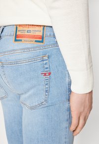 Ljusblå denimjeans med en synlig bakficka. Har en brun etikett med "Diesel Industry" och en liten röd logoakcent.