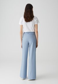 Pantalon large bleu clair avec une texture lisse et une taille élastique, comportant une seule poche arrière. Associé à un t-shirt blanc uni.
