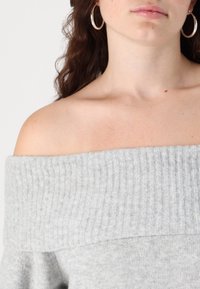 Svetlo siva, rebrasta pulover brez ramena z ohlapnim krojem. Mehka tekstura, z širokim izrezom in gladkimi robovi.